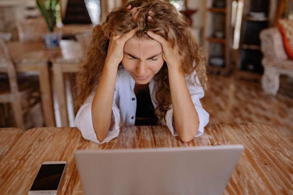 A woman has her hands on her head as she appears to struggle with working on her laptop.