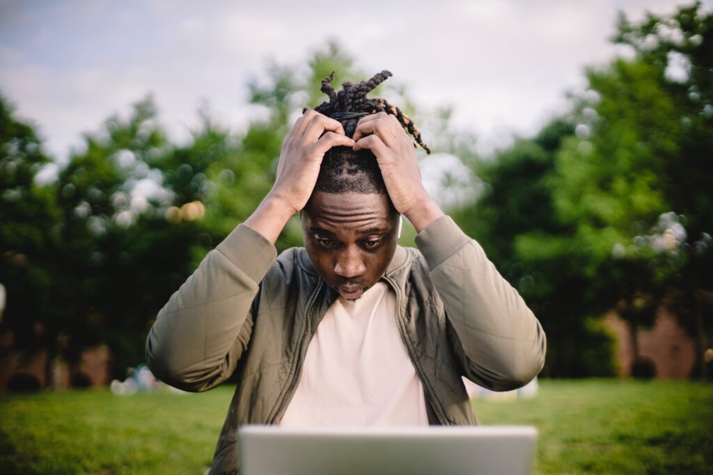 A man has his hands on his head as he looks down on his laptop.